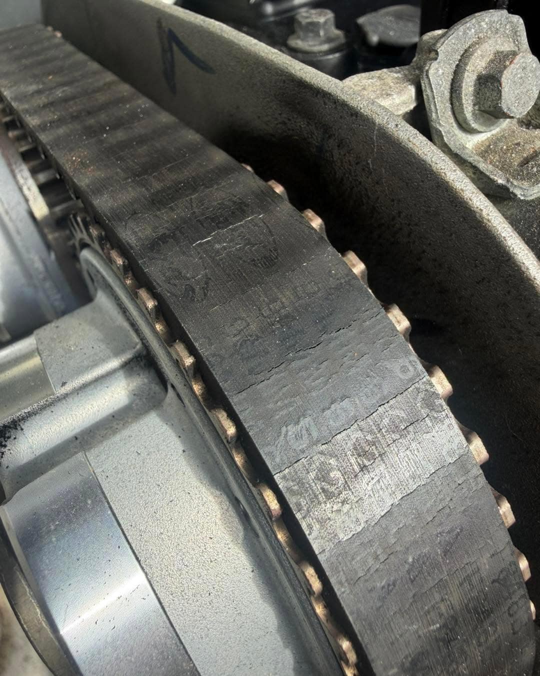 Close-up of a timing belt still on the engine, its face scuffed and worn, with inspection marks on it.