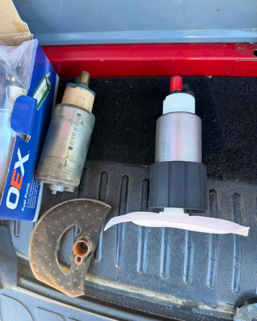An old fuel pump on the left beside a new fuel pump and its box on the right, laid on a ribbed liner.