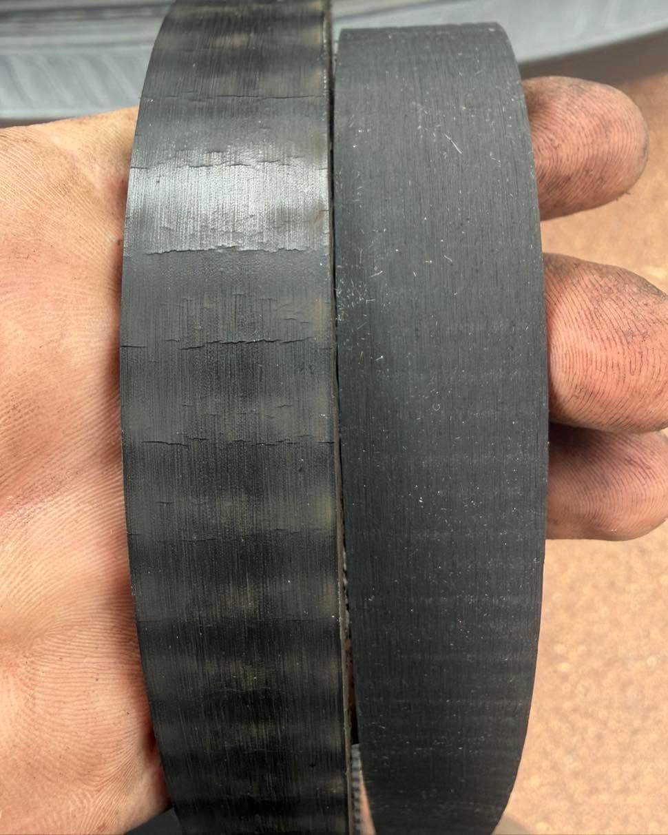 Two timing belts held side by side in a hand: the left one scuffed and worn, the right one uniform and new.