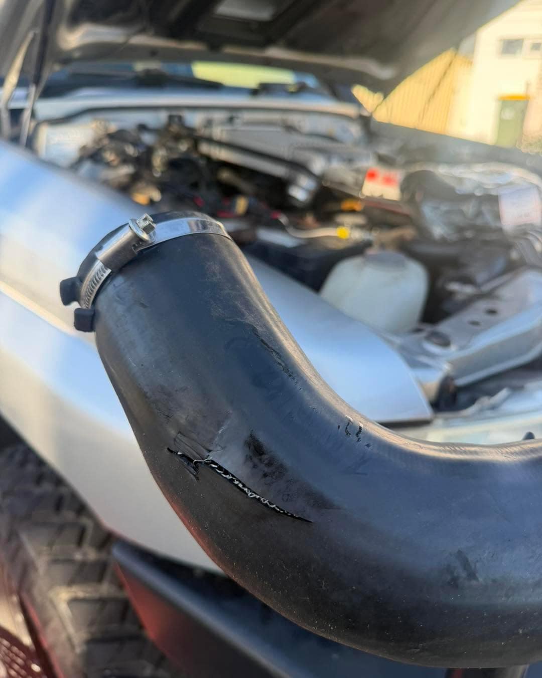 Close-up of a black turbo boost hose with a visible split along its bend, a hose clamp at the end.